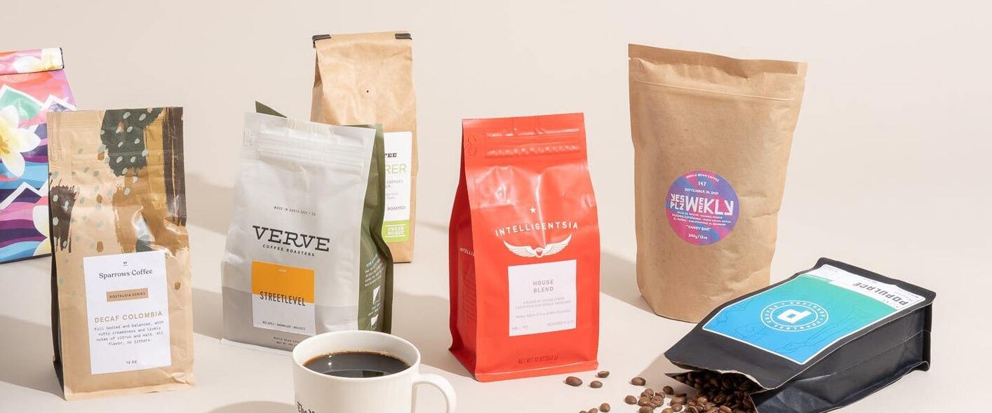 Printed stand-up coffee bags with degassing valves on a studio table beside a cup of coffee
