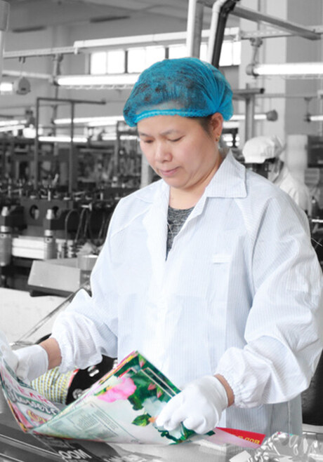 Operator checking a printed pouch against the approved proof on the bag-making line